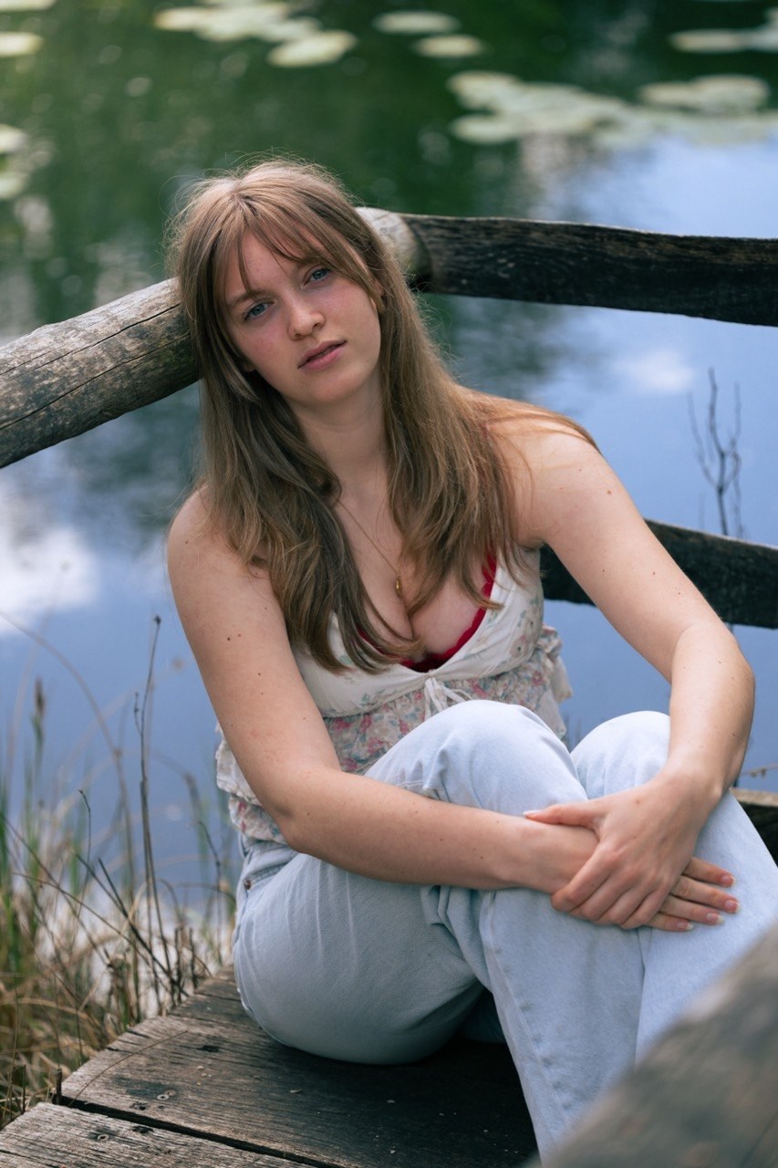 Woman seated beside a pond and wooden railing in natural light
